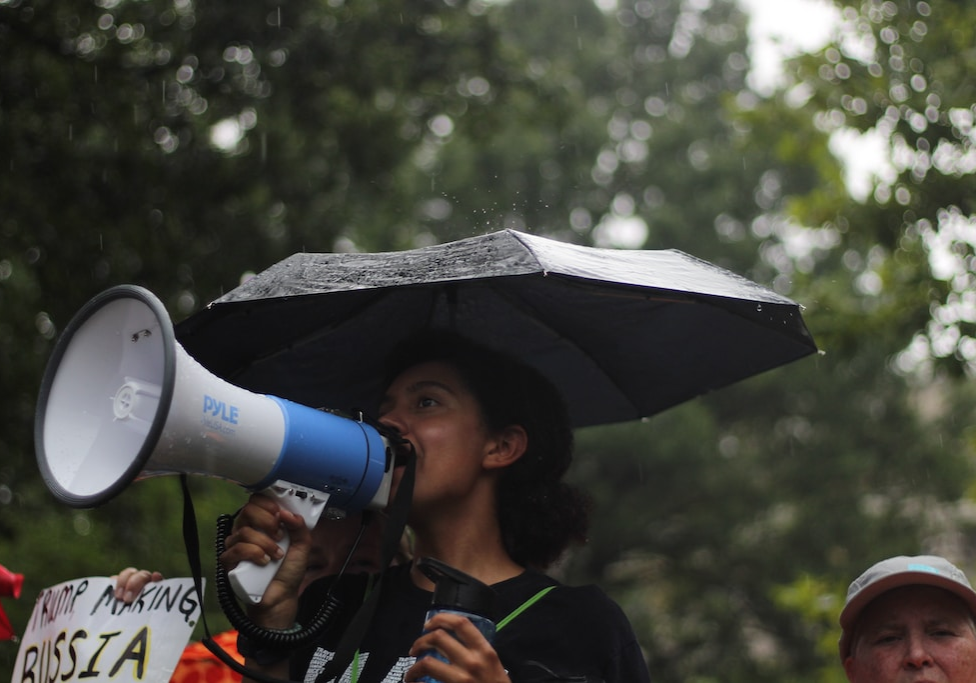 woman standing holding umbrella and white megaphone during daytime